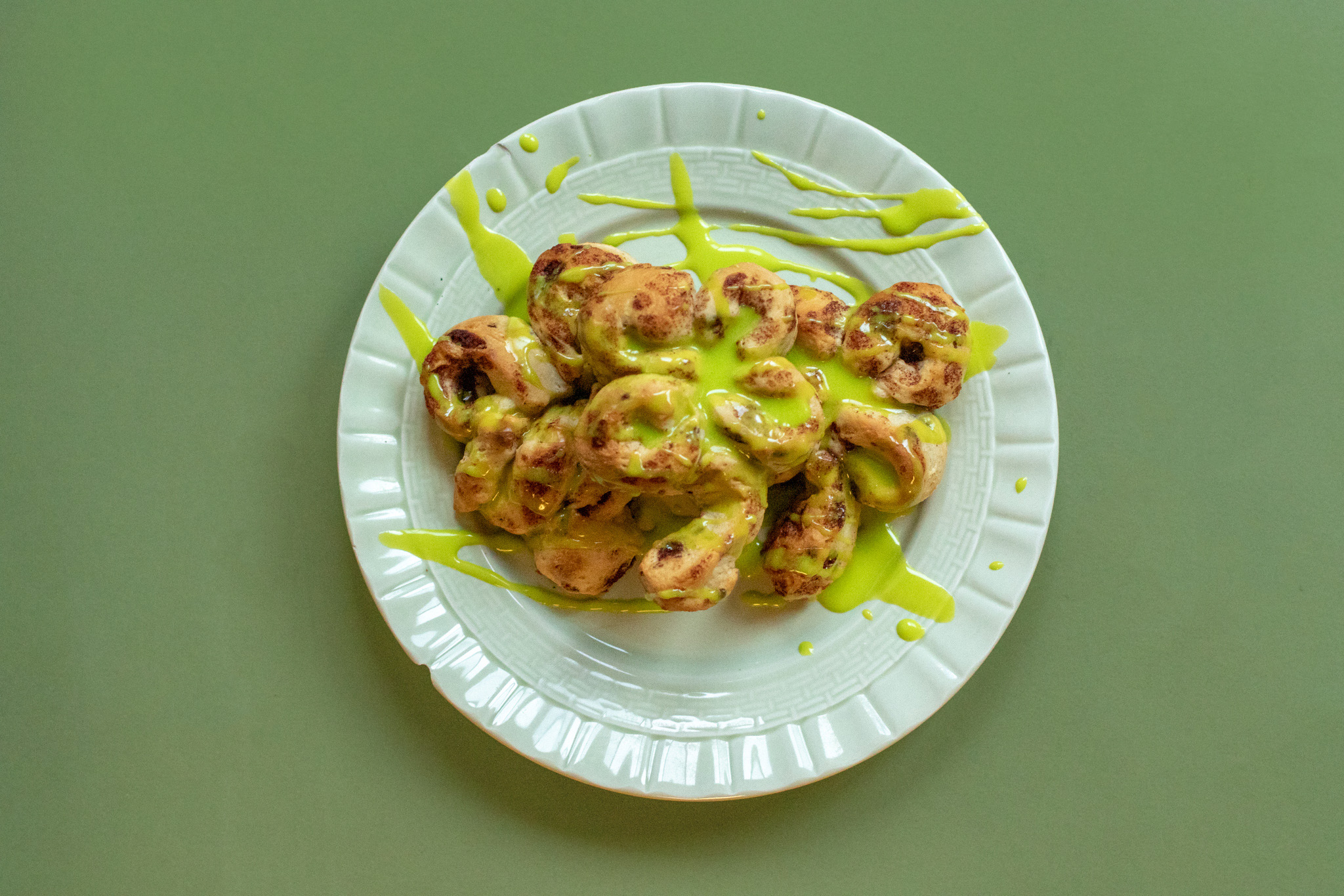 cinnamon rolls in the shape of four leaf clovers on a green plate with a green backdrop. Green frosting is spread all over the cinnamon rolls.